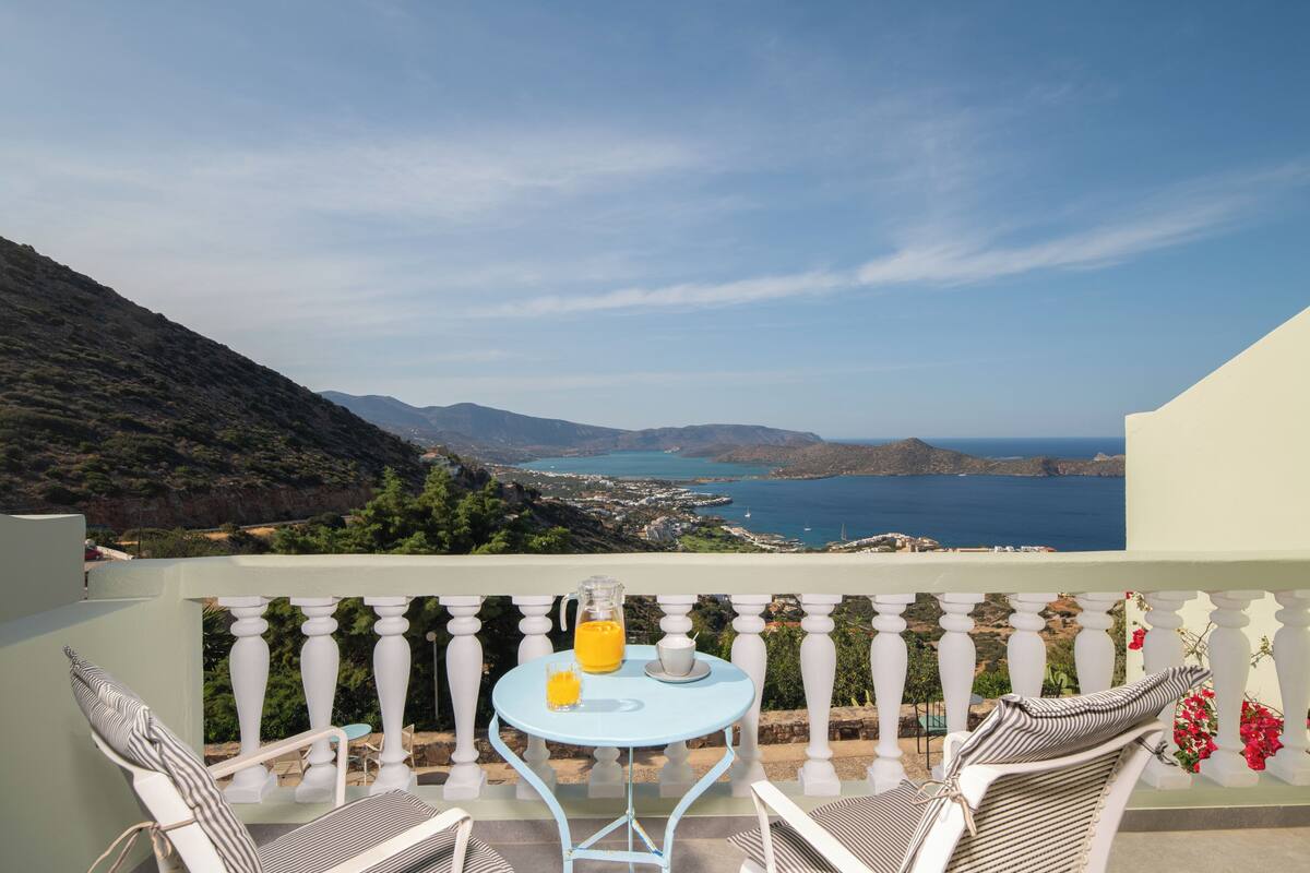 A balcony with a table, two chairs, a pitcher of orange juice, and a glass of water.