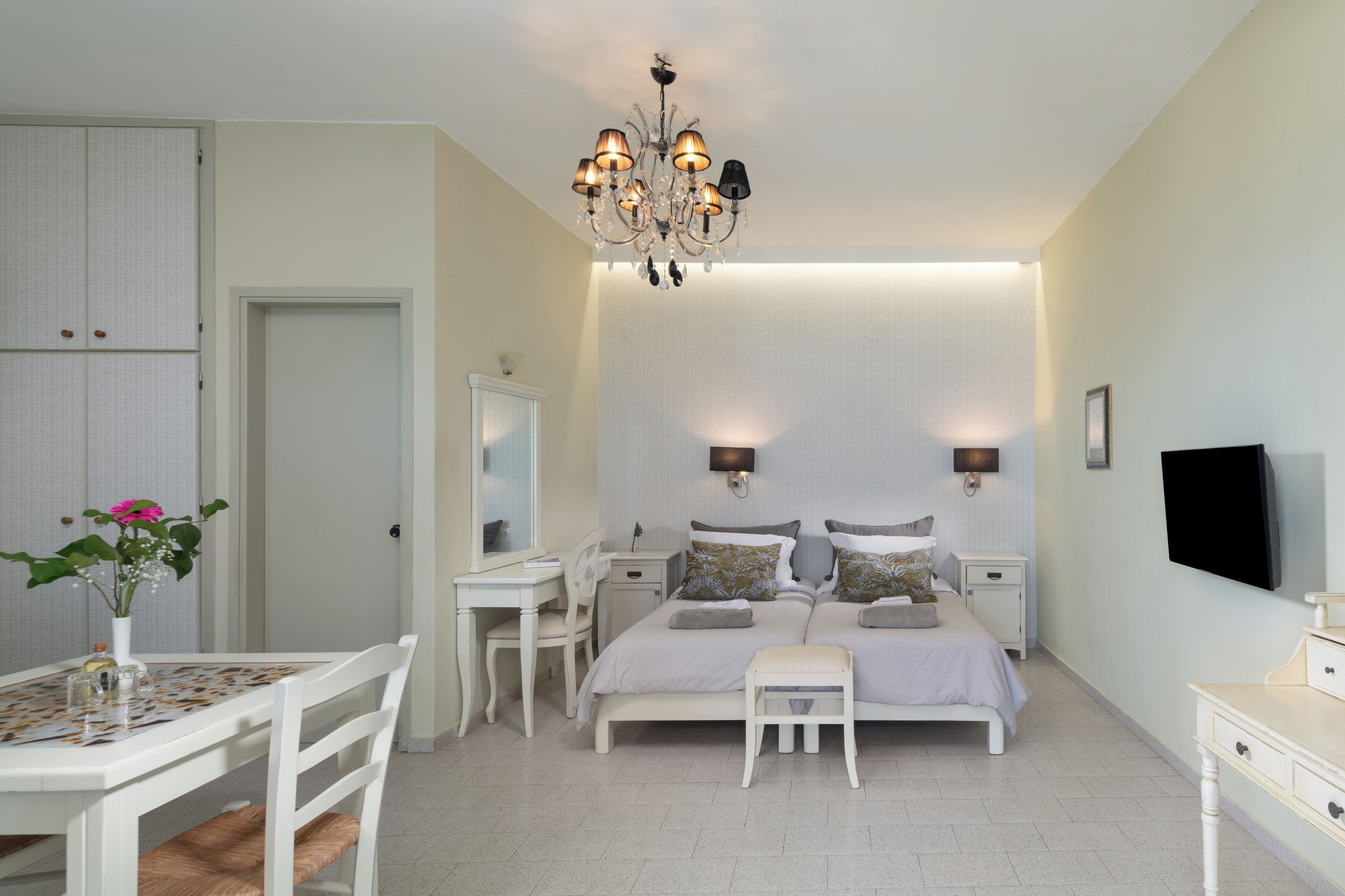 Une chambre à coucher comprenant un lit, des tables de chevet, un bureau, une chaise, un téléviseur et un lustre.