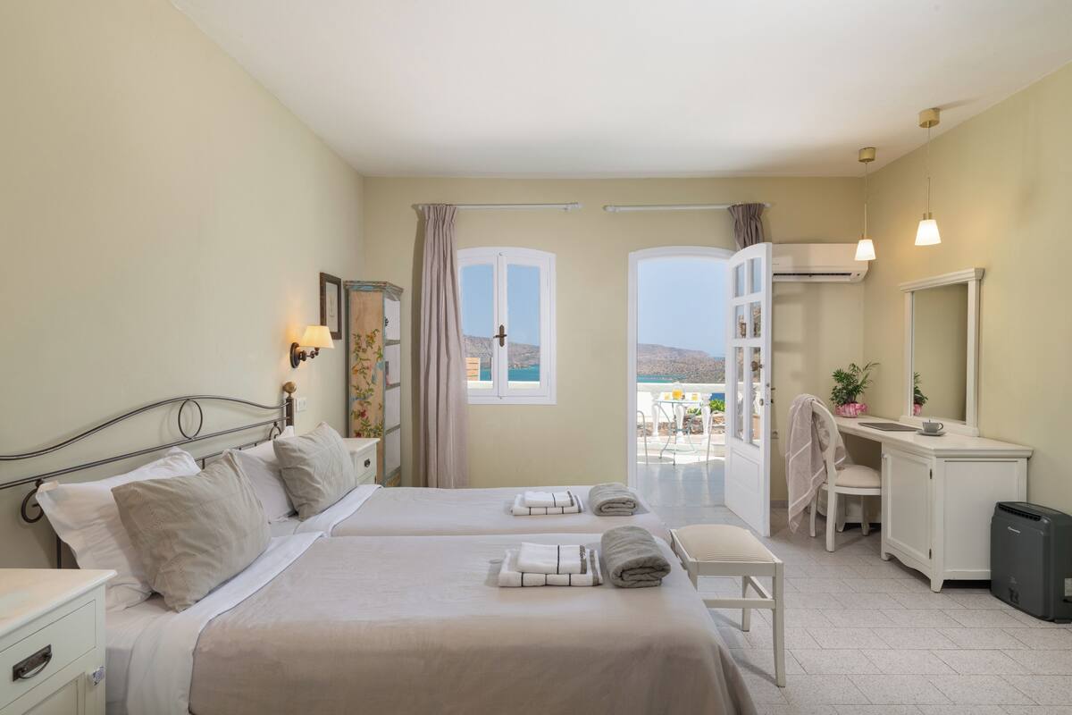 A hotel room with two beds, a balcony with a view, a desk, and a chair.