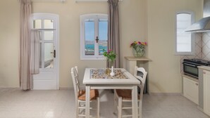 A kitchen with a dining table, chairs, a window with a view, a small cabinet, and a stove. - Adrakos Apartments - Adults Only (Agios Nikolaos)