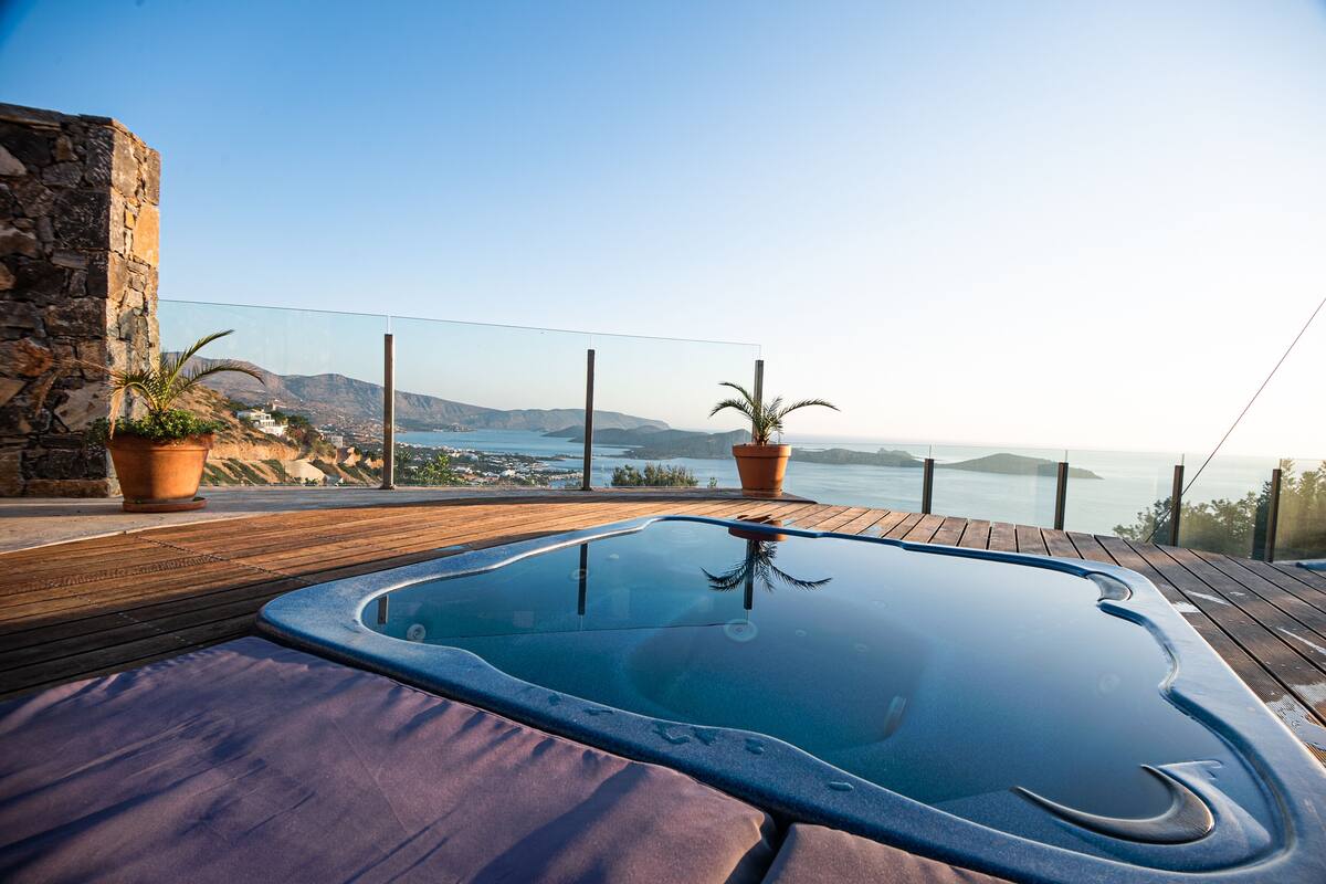 A hot tub on a wooden deck with a view of the sea and mountains.