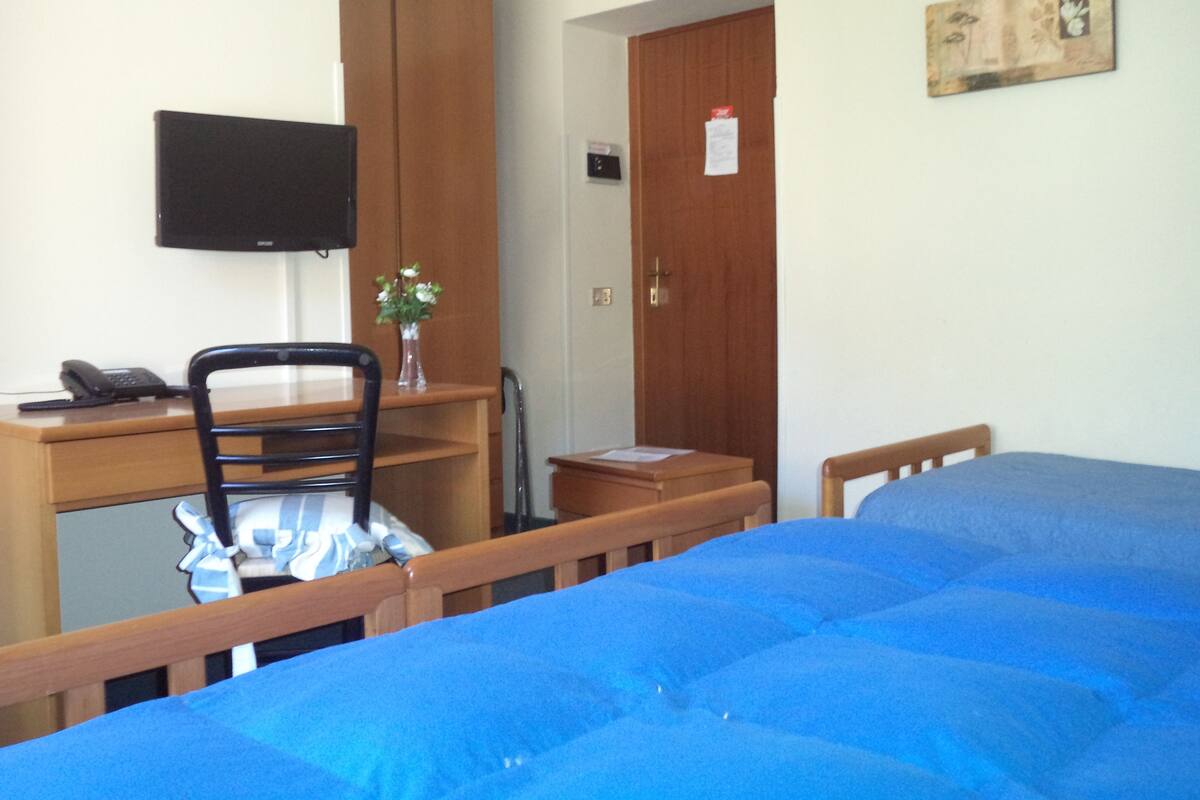 A bedroom with a bed, a desk with a chair, a television, and a wooden wardrobe.