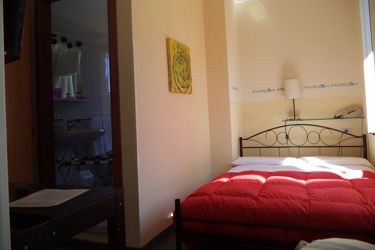 A bedroom with a bed, a bedside table, a mirror, and a wall-mounted lamp.