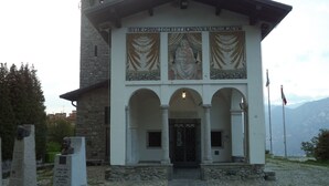 Un edificio con fachada blanca, una torre de campanas y un mural sobre la entrada.