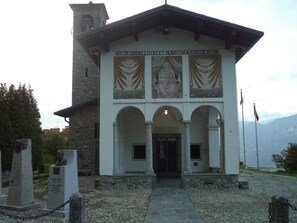 A building with a white facade, a bell tower, and a mural above the entrance. - Hotel Il Nibbio (Magreglio)
