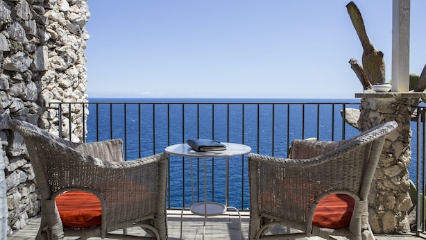 A balcony with wicker chairs, a small round table, and a view of the sea. - Hotel Piccolo Mondo (Castro)