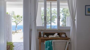 Una stanza con vista sul mare, una scrivania in legno con un libro, una tazza e una piccola pianta.