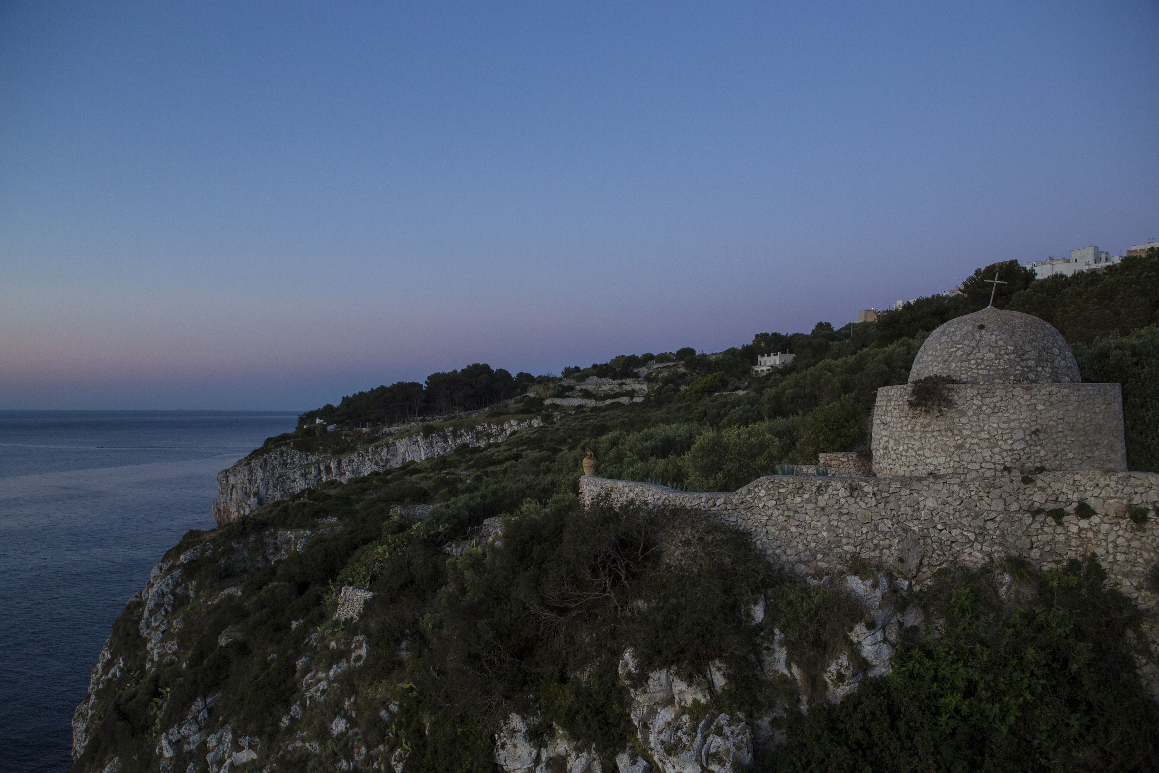 A stone structure with a dome and cross on a cliff overlooking the sea.