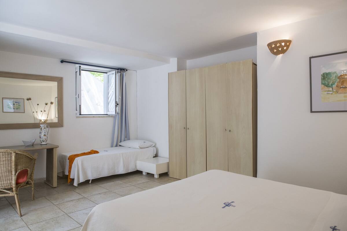 A bedroom with a bed, a desk, a chair, a wardrobe, and a window with curtains.