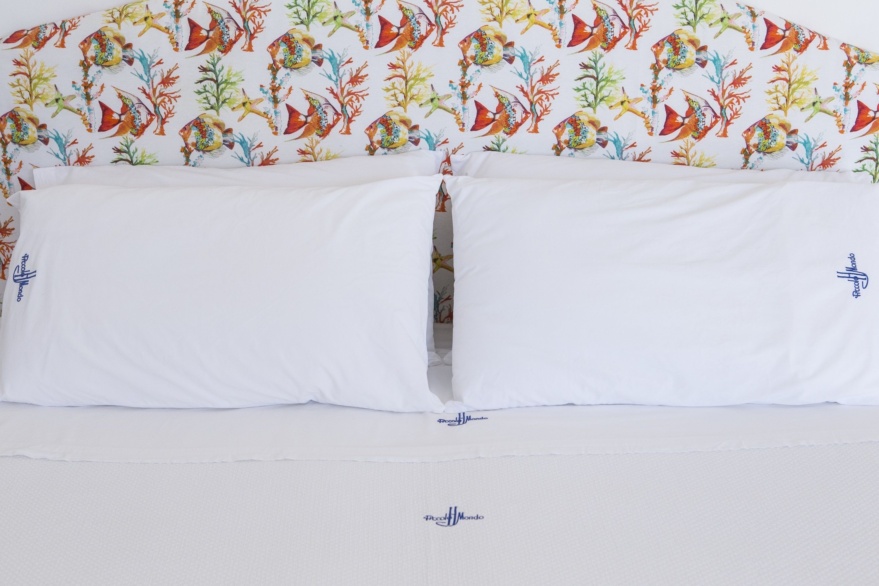 Una cama con sábanas blancas y un estampado de peces de colores en la pared de fondo.