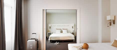 Une chambre d’hôtel avec un lit, une valise, un chapeau et une pancarte sur le mur portant l’inscription « ST. SAUVEUR ».