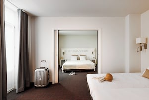 Une chambre d’hôtel avec un lit, une valise, un chapeau et une pancarte sur le mur portant l’inscription « ST. SAUVEUR ».