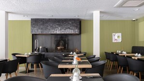 A modern dining area with black chairs and tables, a central black wall with a textured pattern, and a green accent wall.