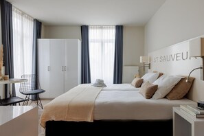 A hotel room with a bed, two bedside tables, a desk with a chair, a wardrobe, and a window with curtains. - Hotel Saint Sauveur by WP Hotels (Blankenberge)