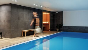 A modern indoor swimming pool with a wooden bench and a person walking by.