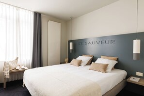 Une chambre d’hôtel avec un grand lit, une table de chevet, une chaise et un panneau fixé au mur sur lequel on peut lire « ST. SAUVEUR ».