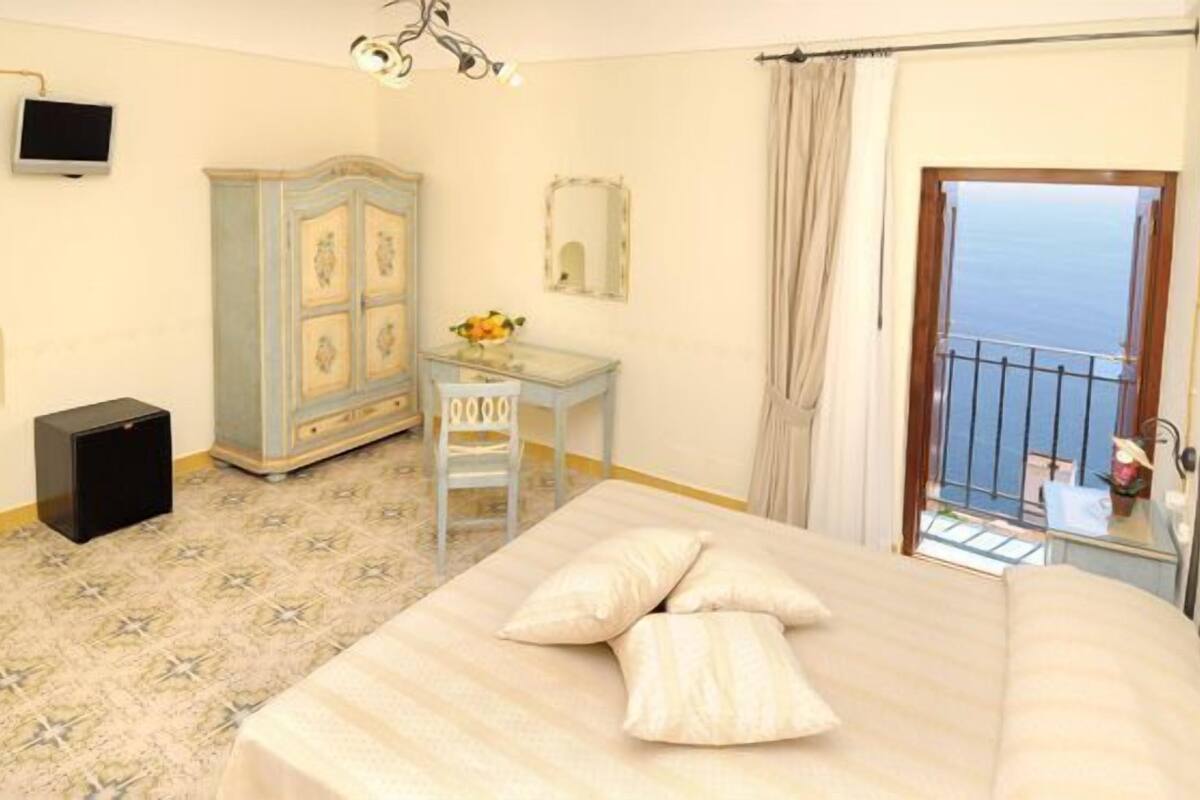 Une chambre avec un lit, un bureau, une armoire, une télévision et un balcon avec vue.