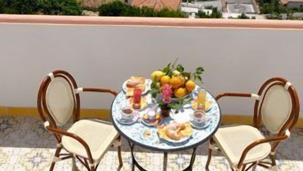 Een balkon met een tafel voor twee, uitkijkend op een kustgezicht met heldere lucht en een verafgelegen vuurtoren.