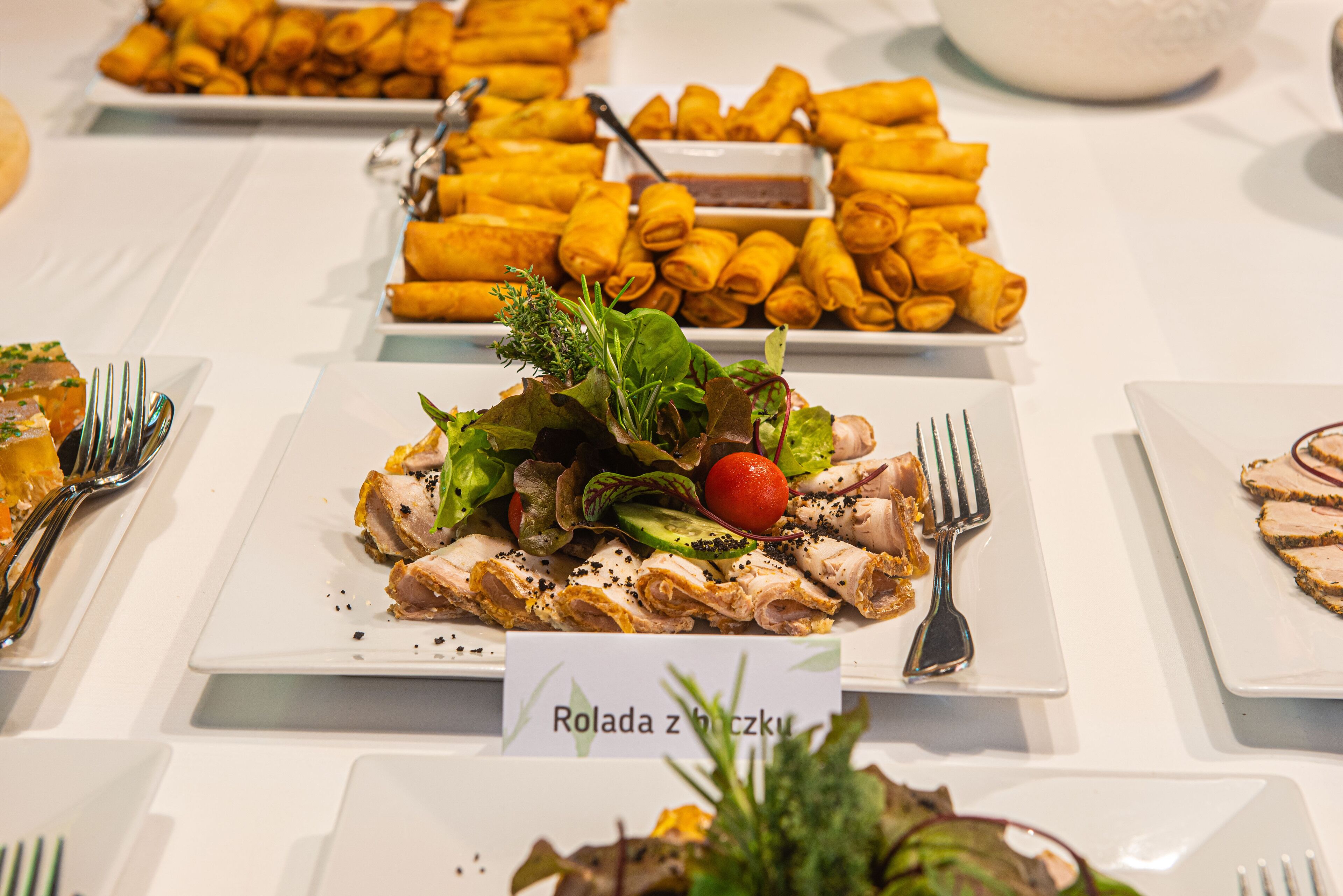 A buffet table with various dishes including spring rolls, salads, and sliced meats.