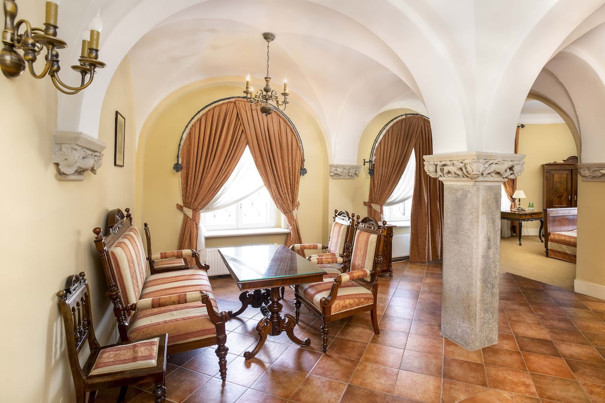 Une salle à manger dotée d’un haut plafond en arc, d’un lustre et d’une grande table entourée de chaises rembourrées.