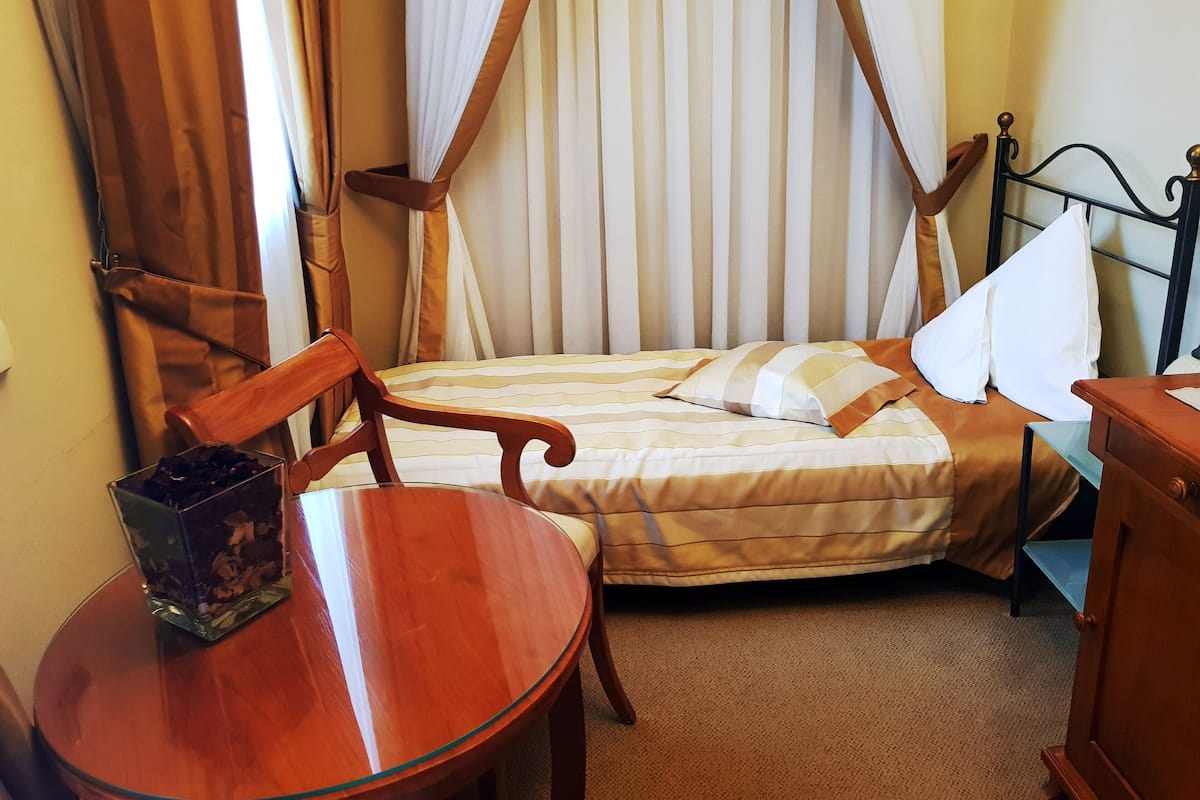 Un lit simple avec un baldaquin, une chaise en bois, une petite table et une table de chevet avec une lampe.
