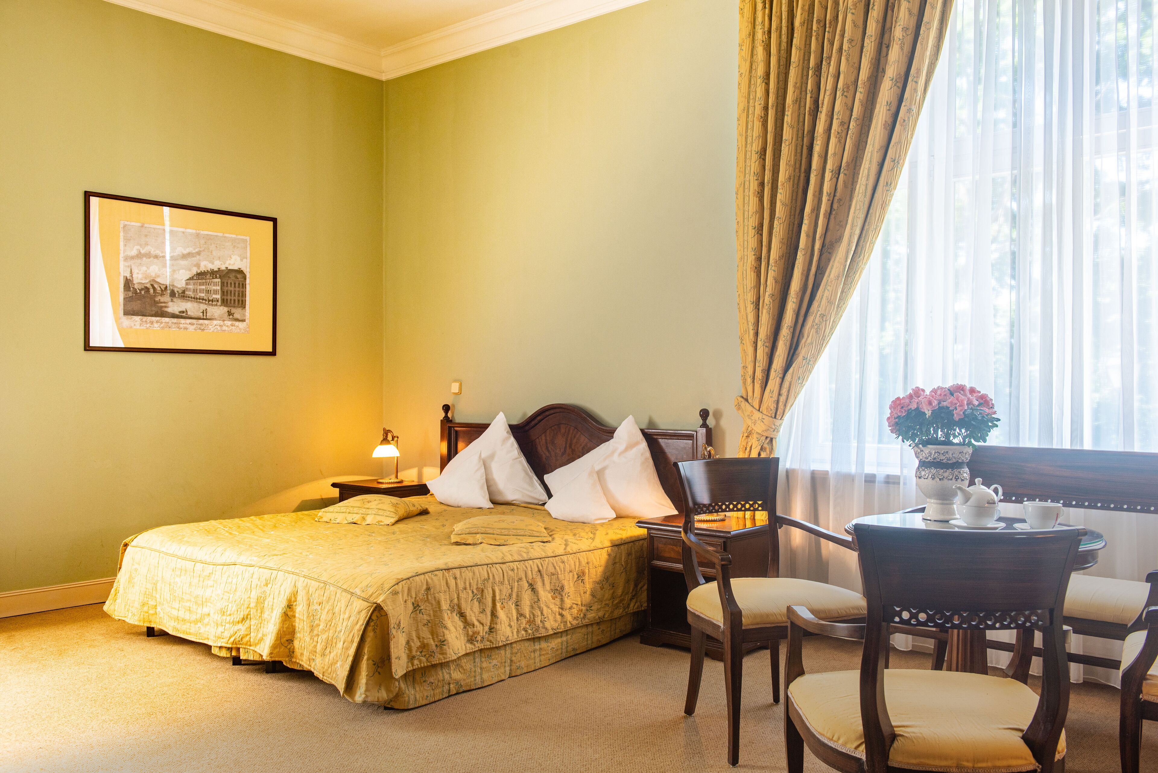 A hotel room with a bed, bedside table, lamp, chair, and a window with curtains.