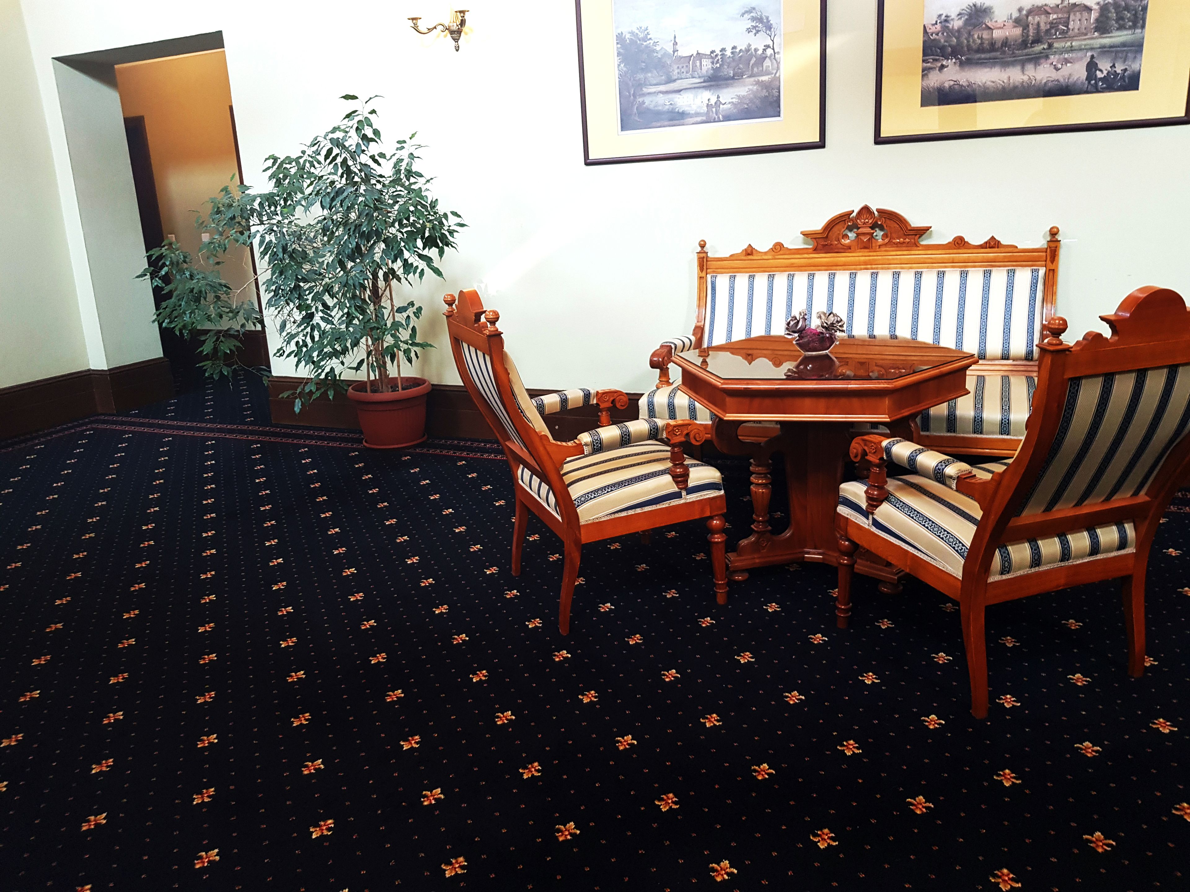 A room with a dark carpet featuring orange floral patterns, a wooden table with a vase, and striped upholstered chairs.
