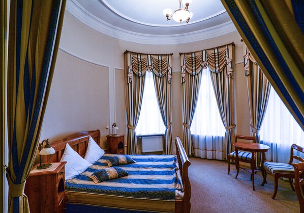 A hotel room with a large bed, two chairs, a small table, and curtains. - Palac Paulinum (Jelenia Gora)