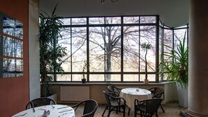 A dining area with round tables, wicker chairs, and potted plants. - Palac Paulinum (Jelenia Gora)