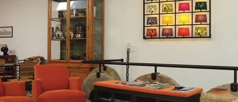 A living room with a wooden cabinet, orange armchairs, a coffee table, and a wall-mounted lamp display.