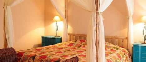 A bedroom with a four-poster bed, two bedside tables, a wicker chair, and a nightstand.