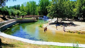 A swimming pool with a stone border, surrounded by trees and a bridge. - Casa do Foral (Rio Maior)