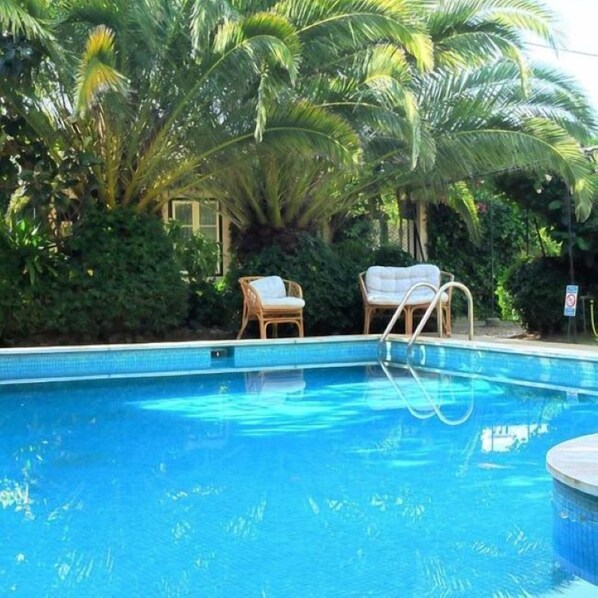 En swimmingpool med krystalklart, blåt vand, omgivet af frodig vegetation og to flettede loungesenge.