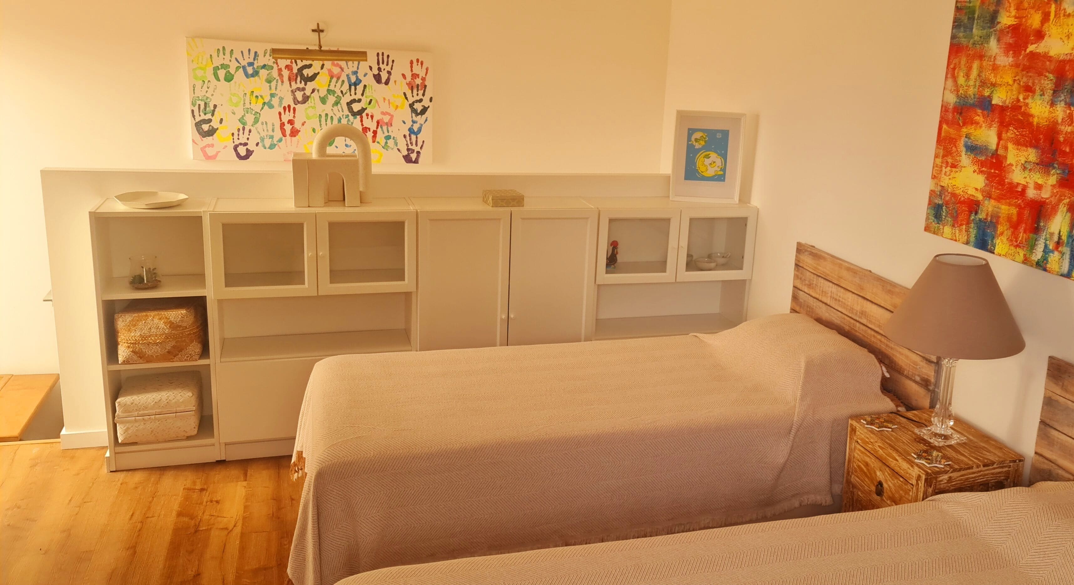 A bedroom with a bed, bedside table, lamp, and a white wardrobe with shelves.