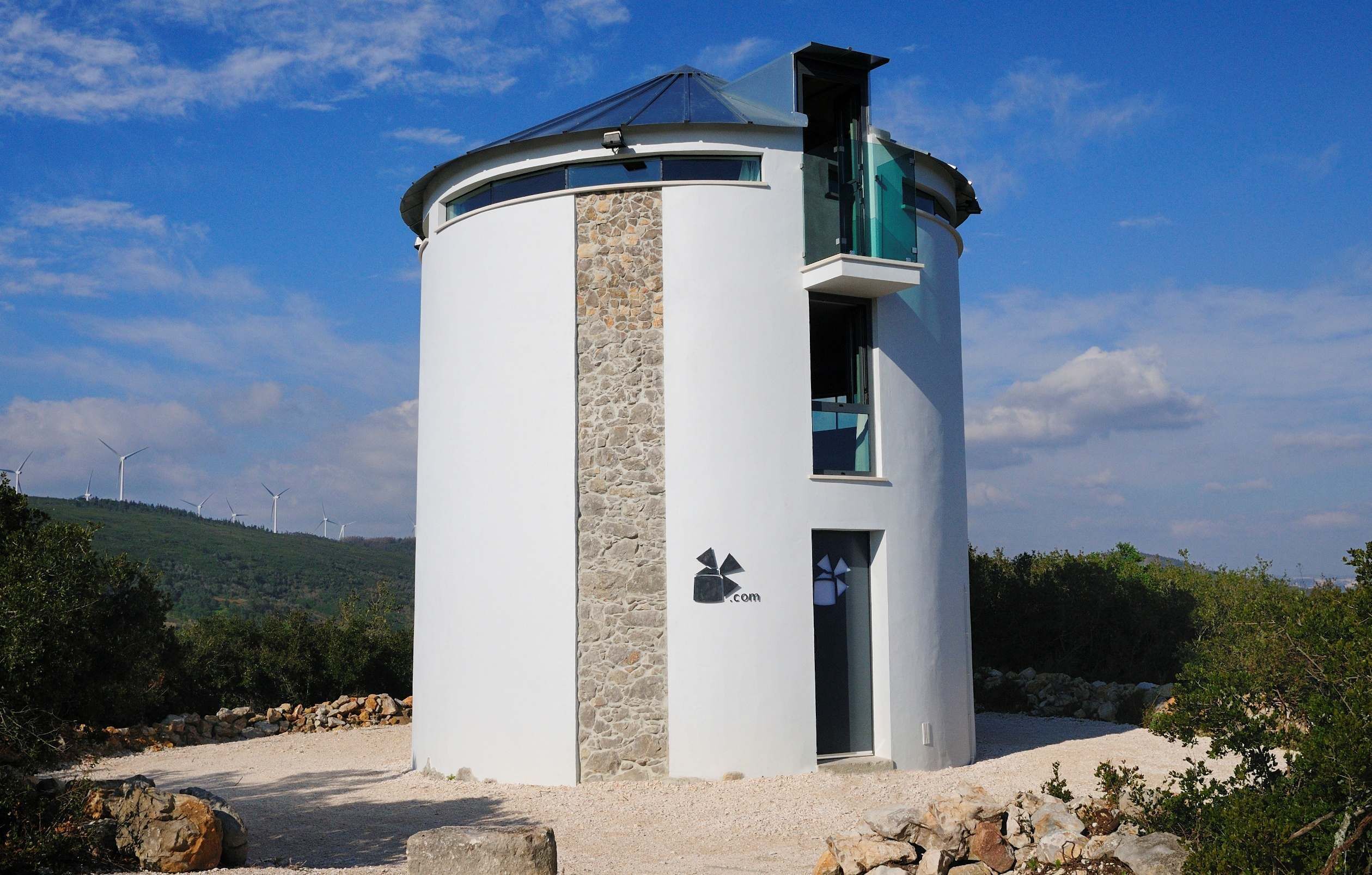 A cylindrical building with a stone facade, a glass balcony, and a door with a logo.
