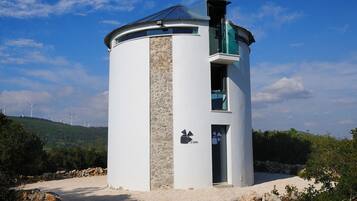 A cylindrical building with a stone facade, a glass balcony, and a door with a logo.