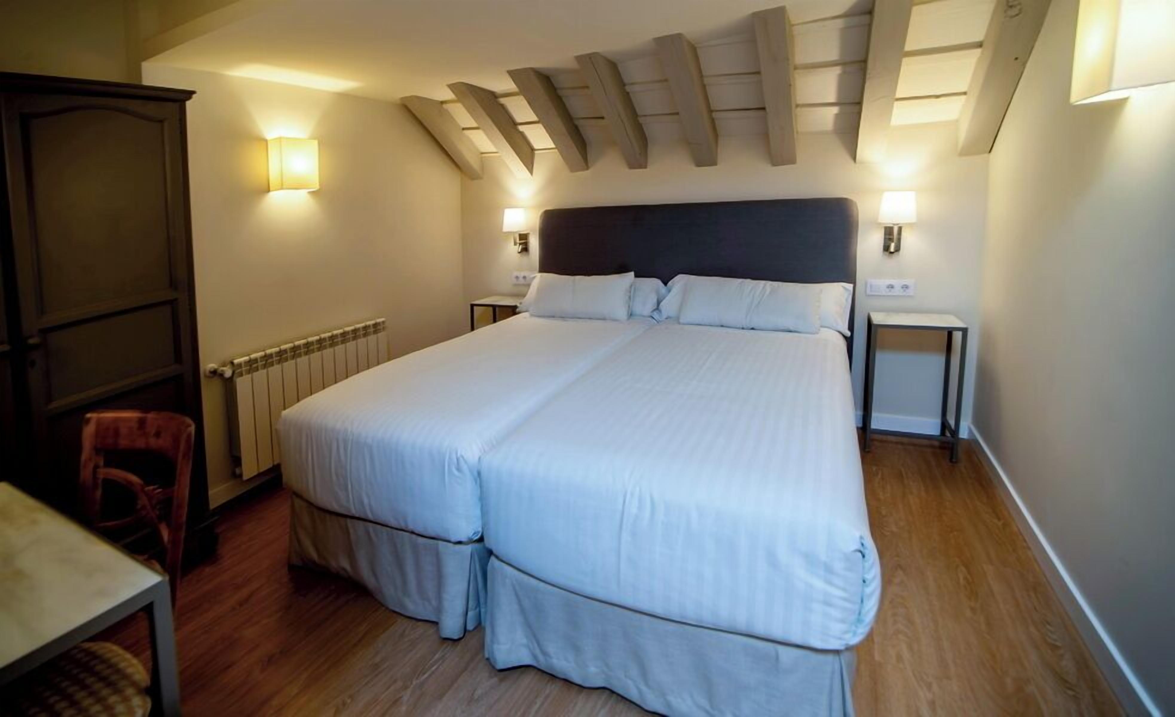 A double bed with a dark headboard, two bedside tables with lamps, a wooden floor, a radiator, and a wooden wardrobe.