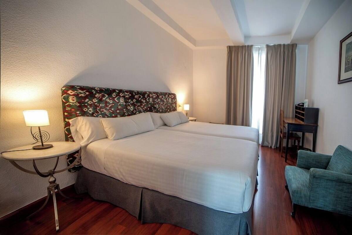 Habitación de hotel con una cama grande, dos mesitas de noche, un escritorio, una silla y una ventana con cortinas.