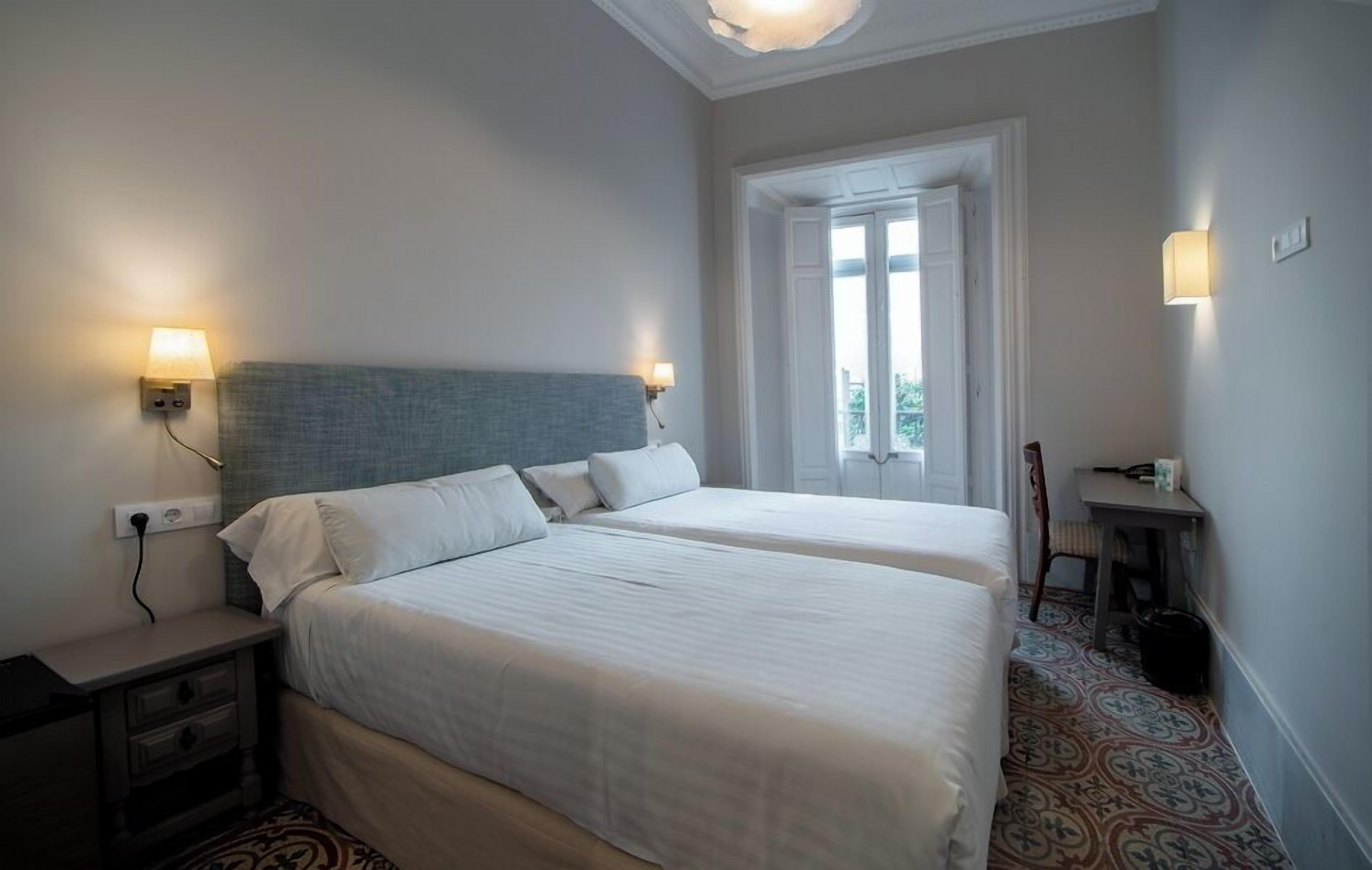 Una habitación de hotel con dos camas, una mesita de noche, un escritorio y una silla.