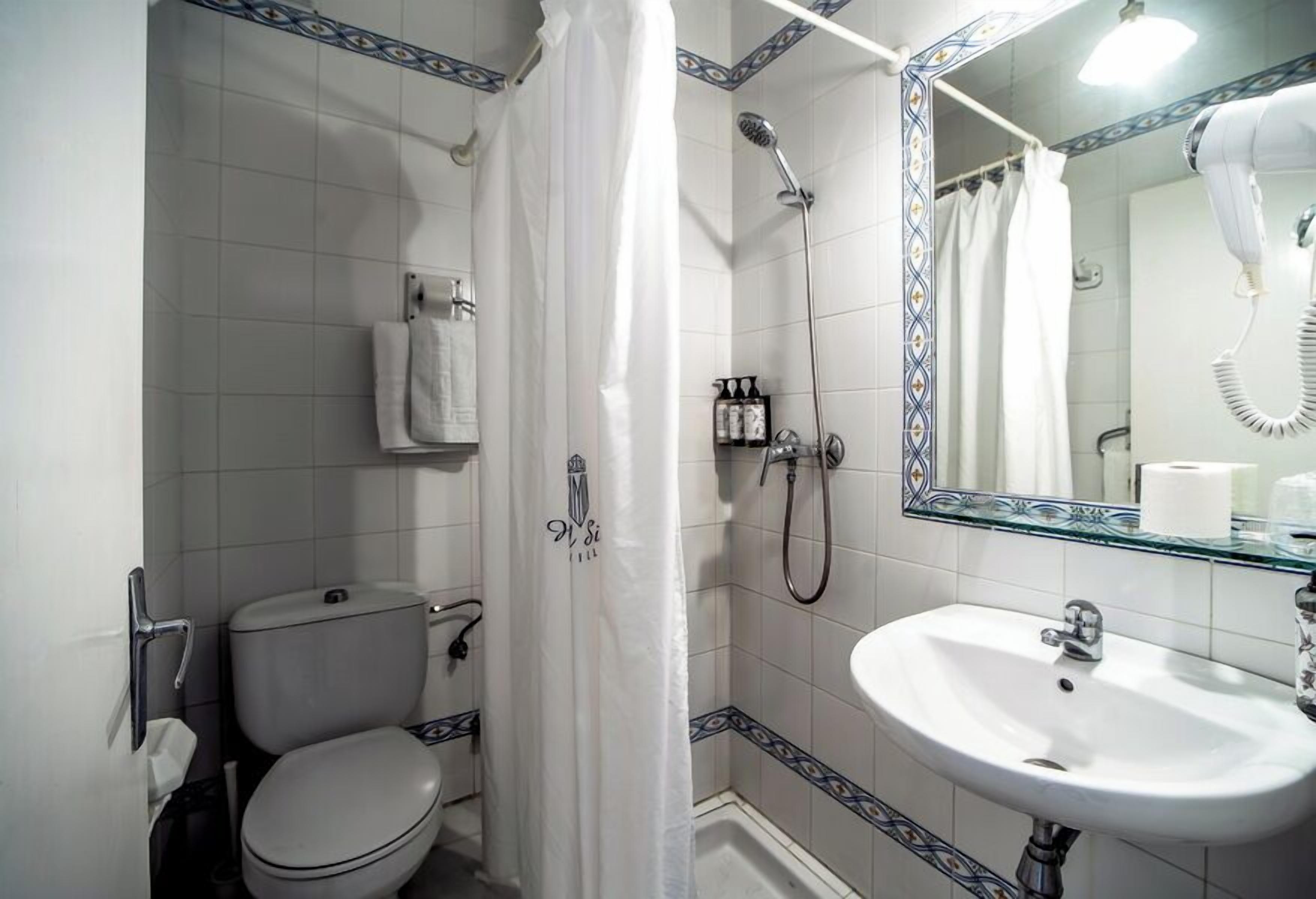 A bathroom with a toilet, shower, sink, and a mirror with a hairdryer.