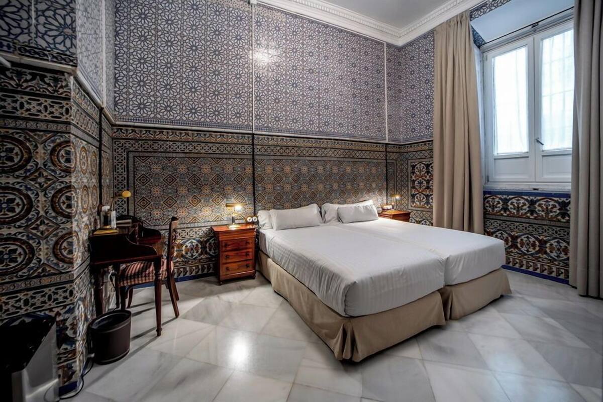 Un dormitorio con una cama grande, dos mesitas de noche, una silla y paredes con diseño.