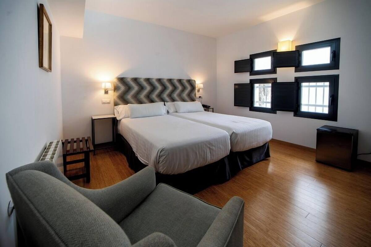 Habitación de hotel con cama doble, dos mesitas de noche, una silla y televisor montado en la pared.