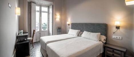 A hotel room with two beds, a nightstand, a dresser, a chair, and a window with a view.