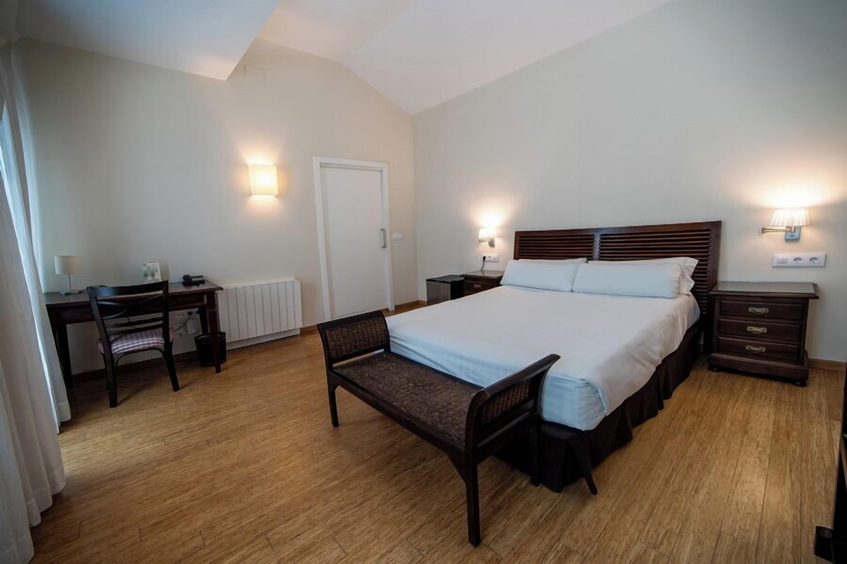 A bedroom with a bed, bedside tables, a desk, a chair, and a radiator.