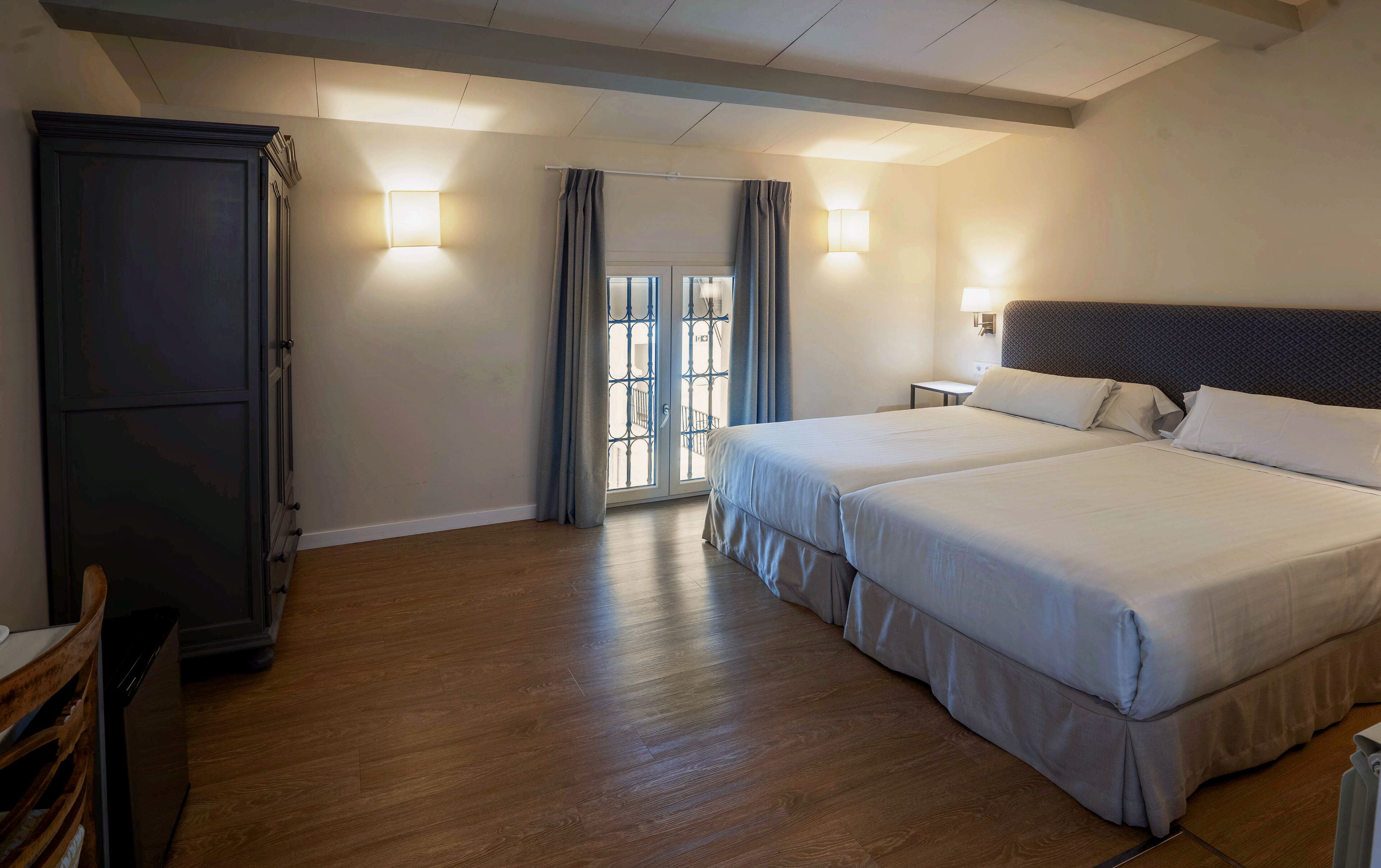 Une chambre d’hôtel avec un lit double, une armoire, une table de chevet et une fenêtre avec des rideaux.