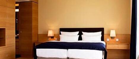 Une chambre d’hôtel avec un lit double, des lampes de chevet, une armoire en bois et un canapé.
