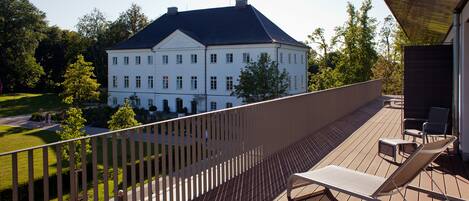 Ein Balkon mit Blick auf ein weißes Gebäude, einer Holzterrasse und zwei Liegestühlen.