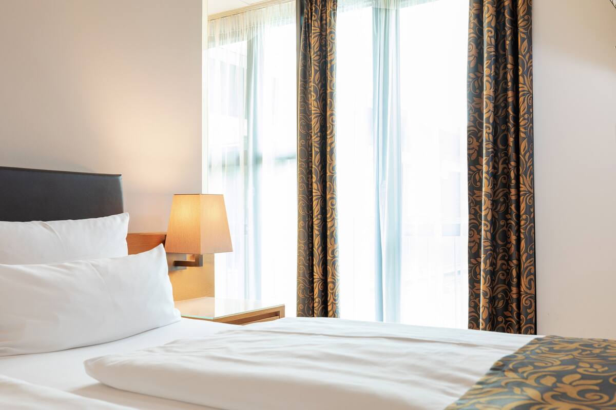 Une chambre d’hôtel avec un lit bien fait, une lampe de chevet et des rideaux à motifs floraux.