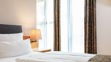 Quarto de hotel com uma cama bem arrumada, abajur e cortinas com padrão floral.