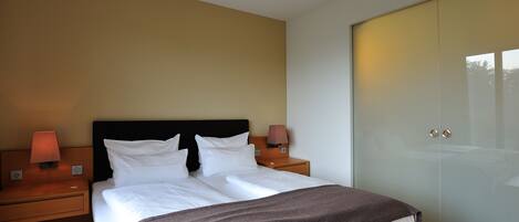 A modern hotel room with a large bed, two bedside lamps, a nightstand, and a wardrobe.